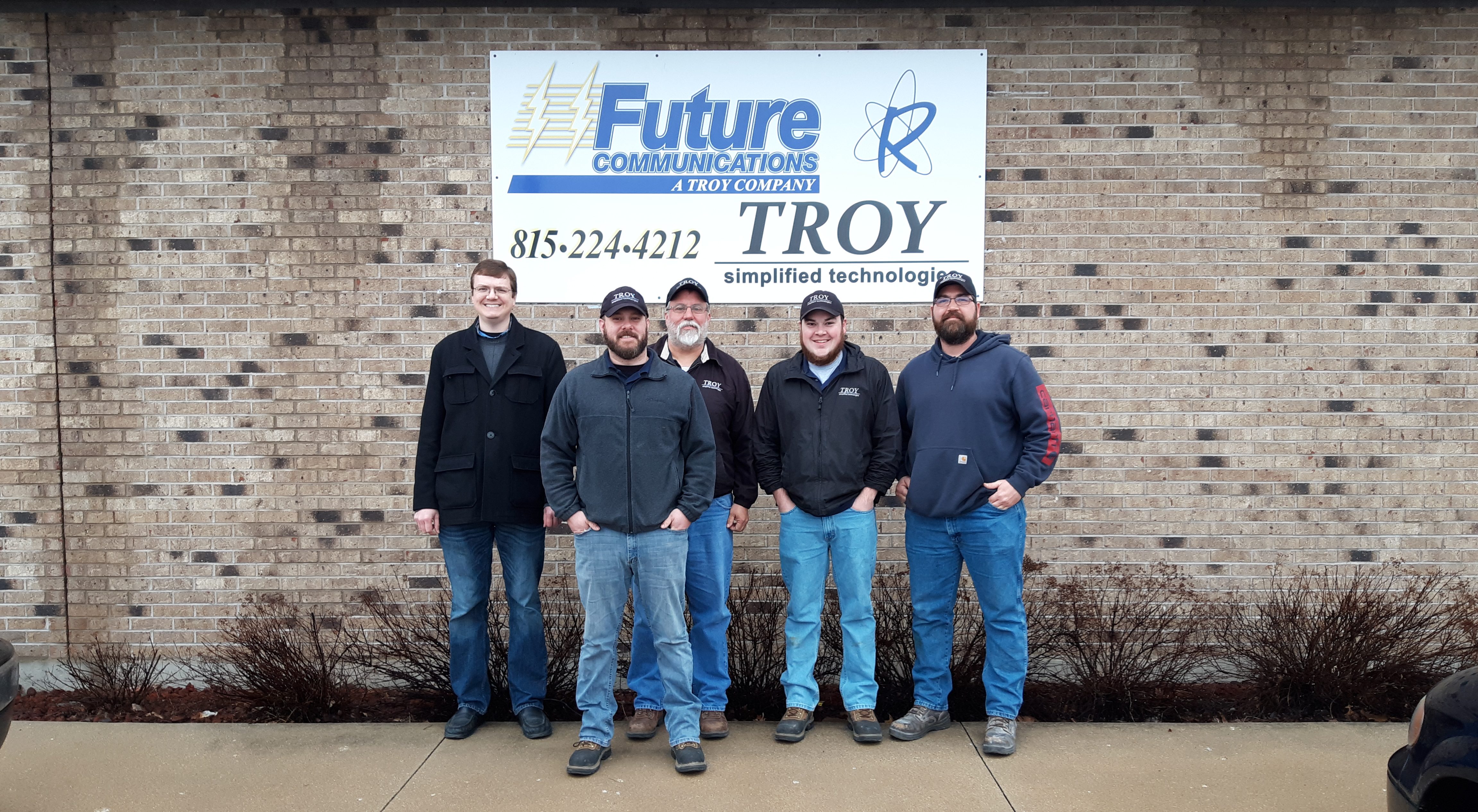 Troy Simptech employees, smiling in front of their logo.